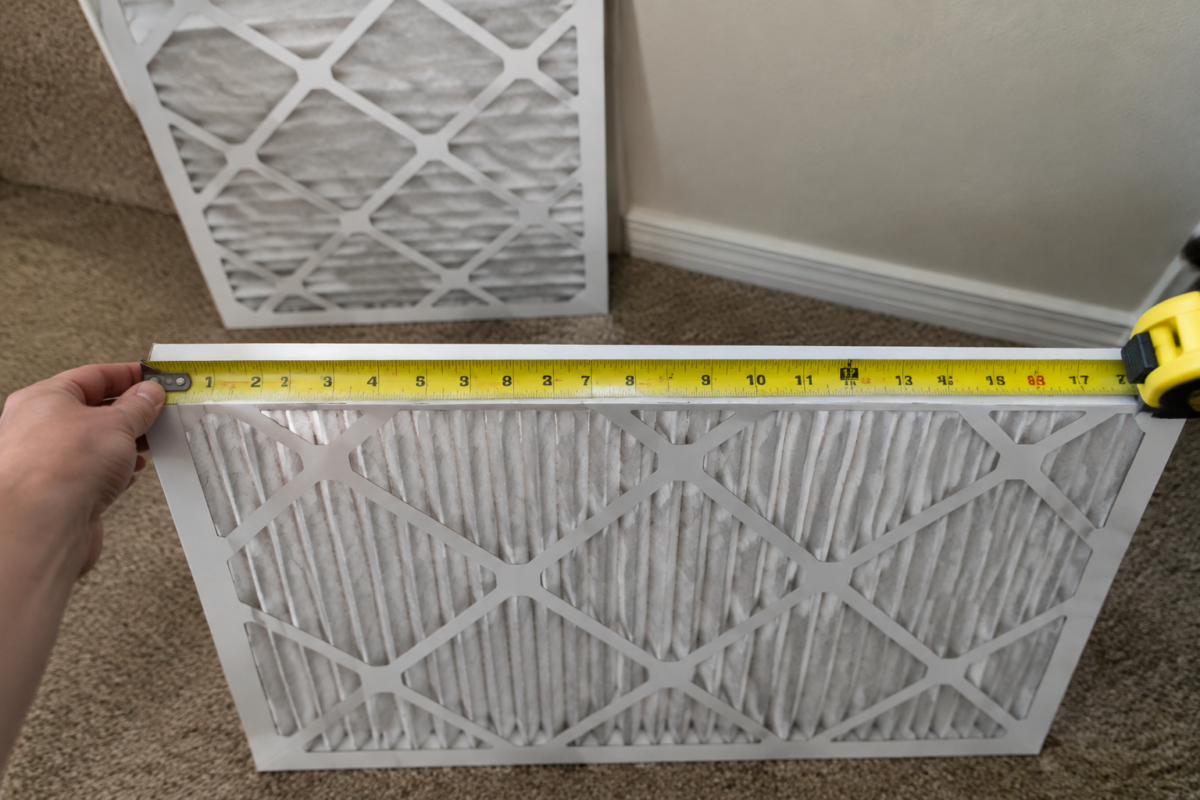 Measuring an HVAC filter with a tape measure to get the actual dimensions