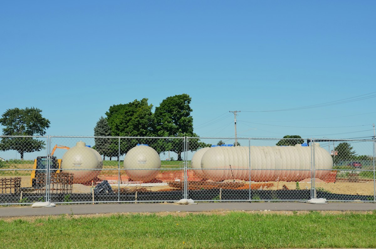 Several large industrial storage tanks behind a chain-link fence