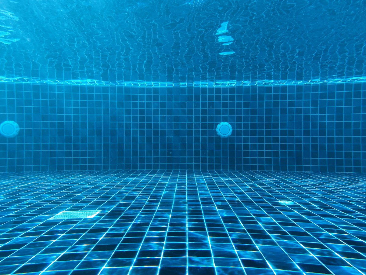 An underwater view of a blue tiled swimming pool with a drain
