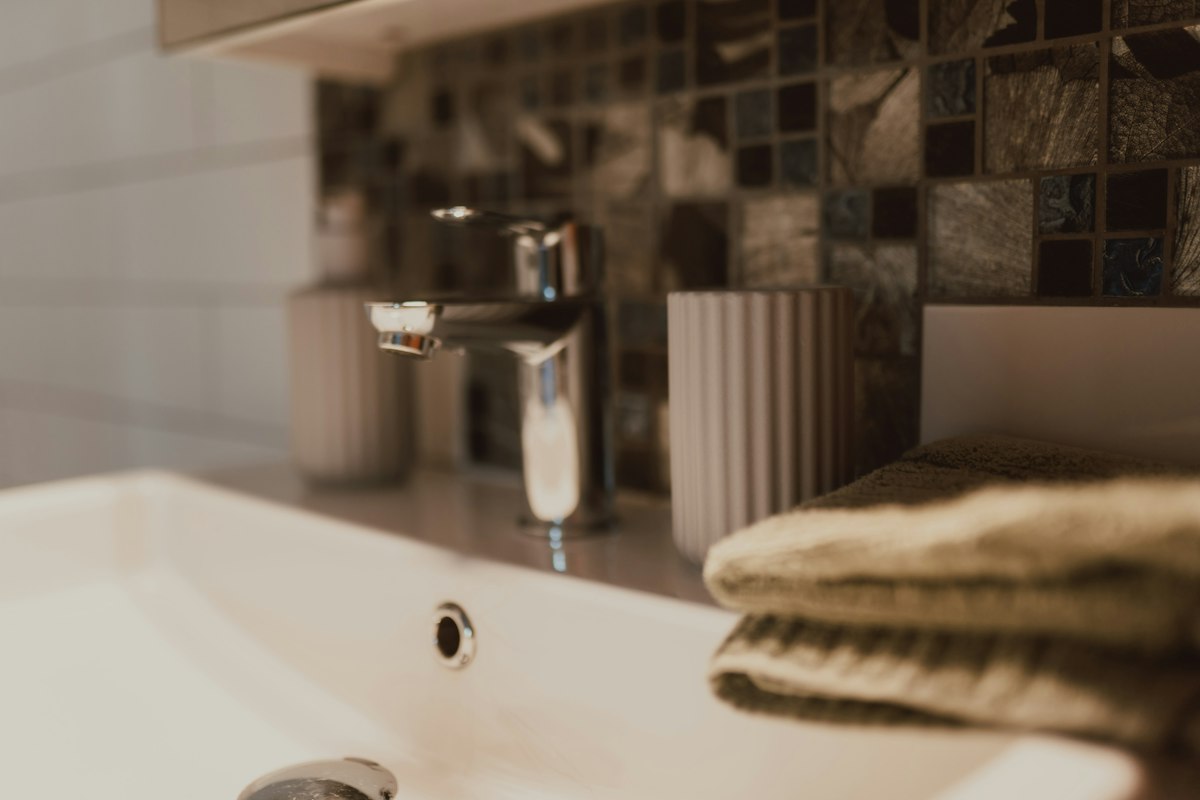 A bathroom sink with a faucet, towels, and mosaic tiles