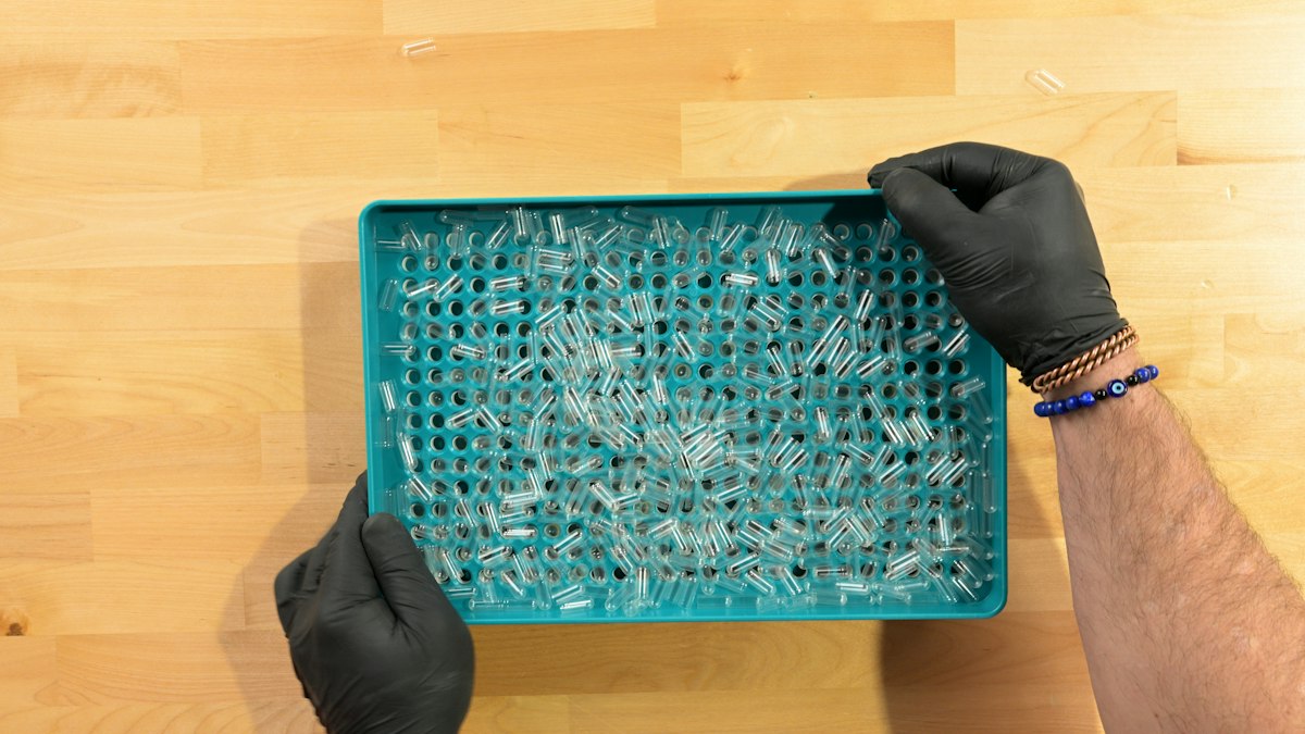 Hands in black gloves holding a tray of capsules