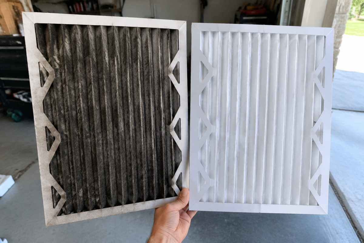 Soot-blackened furnace filter held next to a clean white replacement filter